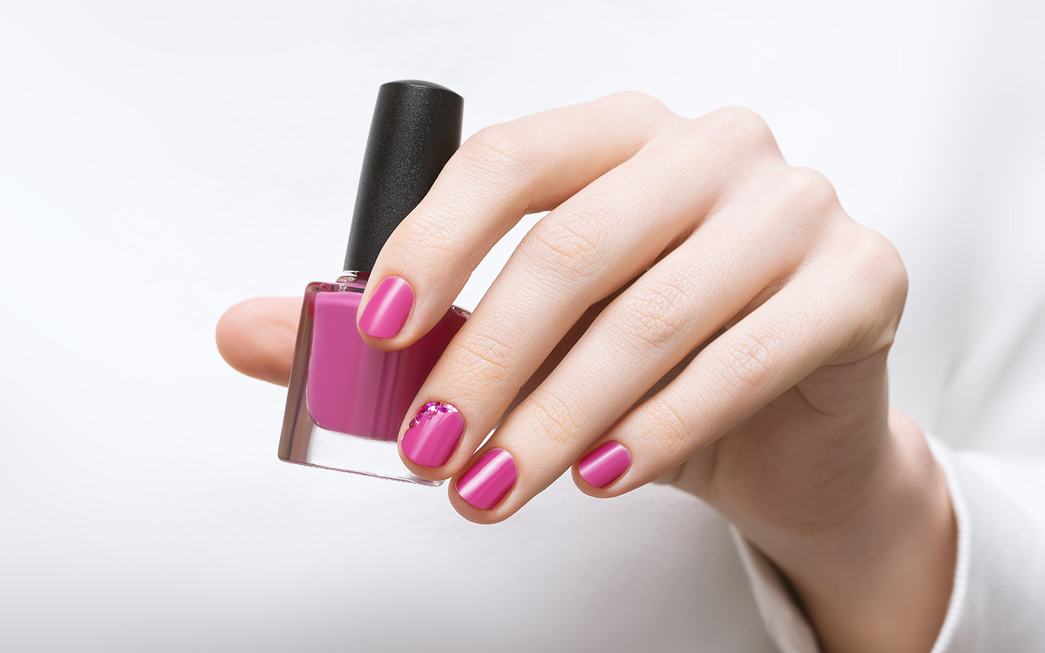 Female hand with pink nail design holding nail polish bottle