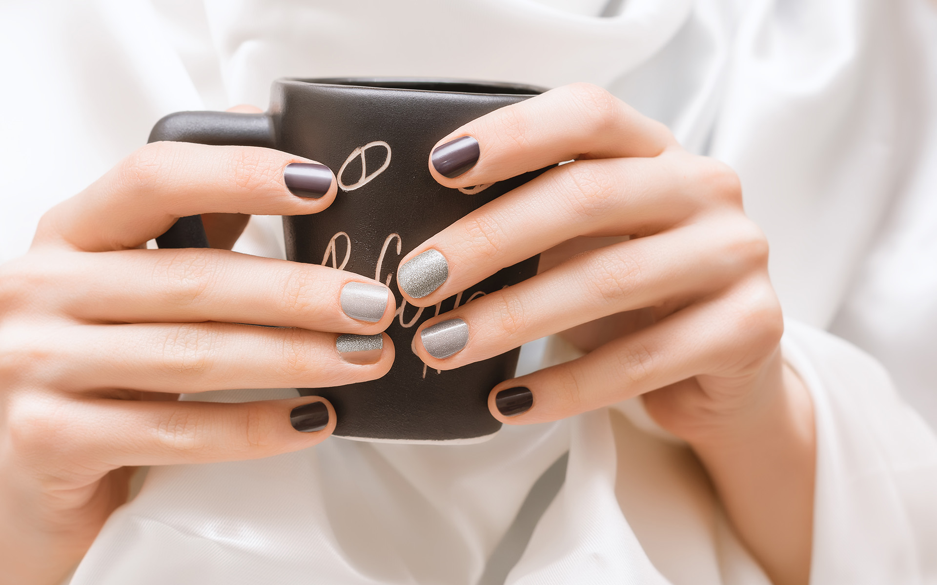 Female hands with glitter nail design holding black cup